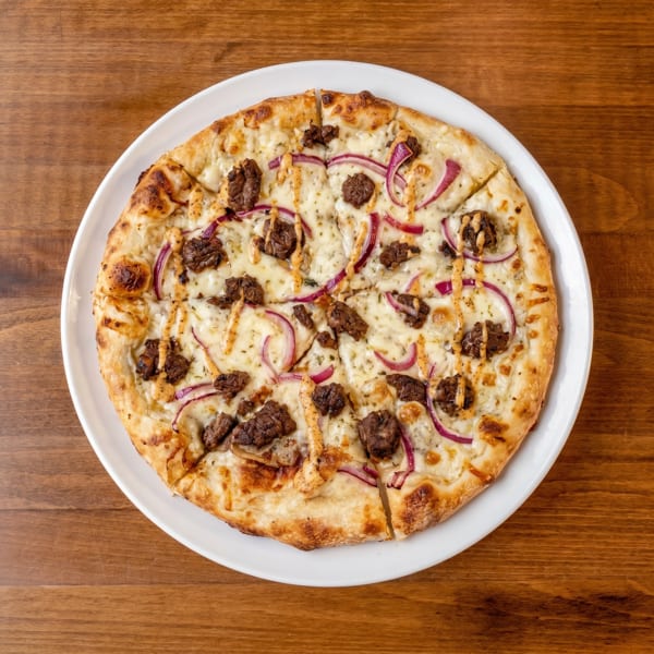 Overhead view of a round pizza with white sauce, beef, red onions, and a drizzle of sauce.
