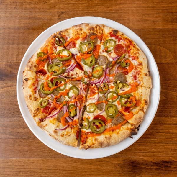 A sliced pizza with pepperoni, sausage, red onion, jalapeños, and orange sauce on a white plate.