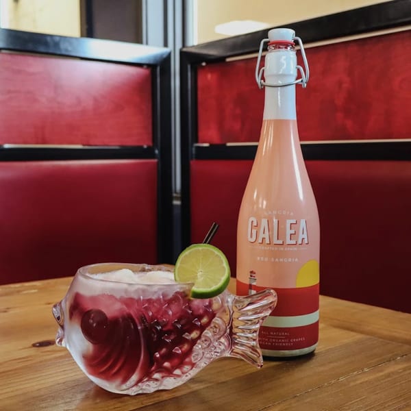 A fish-shaped glass of red sangria with lime and a bottle of Calea Red Sangria.
